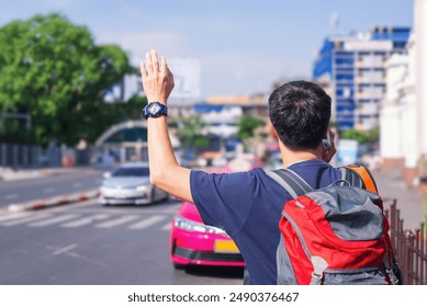Back view of a man with a backpack and a watch hailing a taxi on a bustling city street.