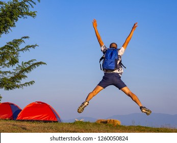 Back view of man backpacker jump up and raising both his arms. Feeling success, unity with nature and freedom. Tourist outdoors enjoying the scenery. Space for text. Freedom and Inspiration Concept.