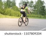 back view of a man with a bicycle and backpack against trees and sky