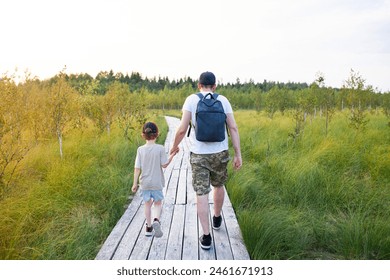 Back view of man with child  walking in wildlife national park. Wooden boardwalk through dried-up swamp with birch trees. Concept of ecotourism, hiking, travel with children. Selective focus . - Powered by Shutterstock