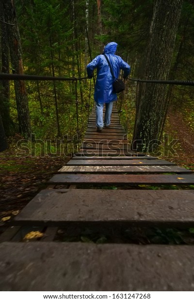 back\
view of man  cross dry river on the wooden suspension bridge. slimy\
dangerous road, way. autumn season. rainy wet\
day.