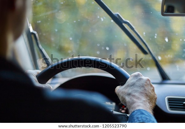 Back view of a man driving a car with moving\
windshield wipers during\
rain.