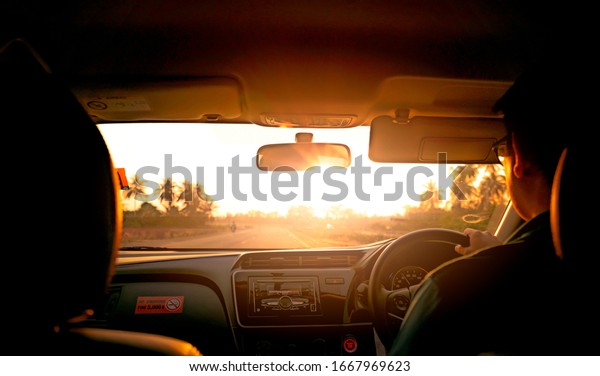 Back view of a man driving car for summer road trip\
travel. Car driving with safety on asphalt road. Driver hand\
holding steering wheel for control car. Inside view of car.\
Dashboard and windshield. 