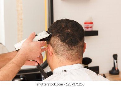 Back view of man getting short hait trimming at barber shop with a clipper machine