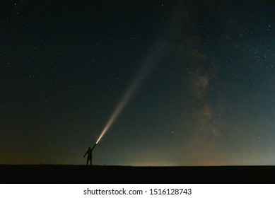 Back view of man with head flashlight standing on green grassy field under beautiful dark blue summer starry sky. Night photography, beauty of nature concept. Wide panorama, copy space background.