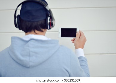 Back view of man with headphones holding mobile smart phone on outdoors background - Powered by Shutterstock