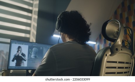 Back View Of Man In Headphones Sitting At The Table And Creating Video Game Hero And 3D Animation In Professional Computer Program, While Working Remotely At Home.