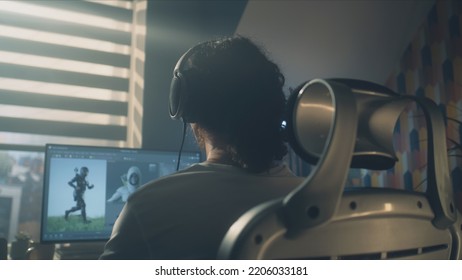 Back View Of Man In Headphones Sitting At The Table And Creating Video Game Hero And 3D Animation In Professional Computer Program, While Working Remotely At Home.