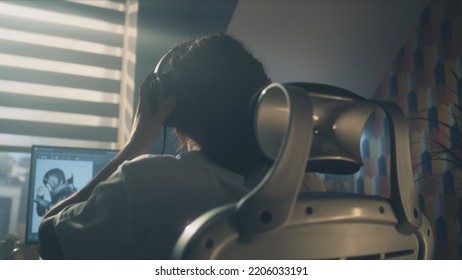 Back View Of Man In Headphones Sitting At The Table And Creating Video Game Hero And 3D Animation In Professional Computer Program, While Working Remotely At Home.