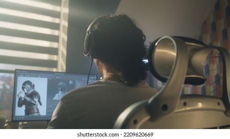 Back View Of Man In Headphones Sitting At The Table And Creating Video Game Hero And 3D Animation In Professional Computer Program, While Working Remotely At Home.