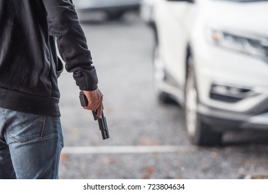 Back View Of Man Holding A Gun In Car Park.