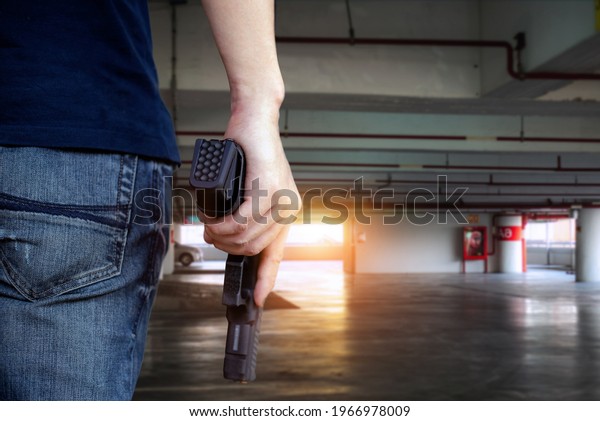 Back view of man holding a gun in car park, copy
space for text.