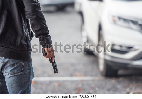 Back view of man\
holding a gun in car park.