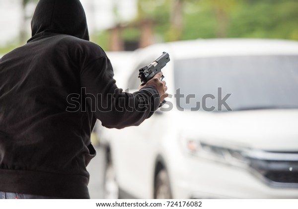 Back view of man\
holding a gun in car park.