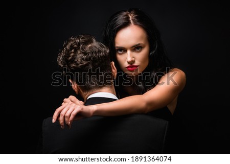 back view of man hugging seductive woman looking at camera isolated on black