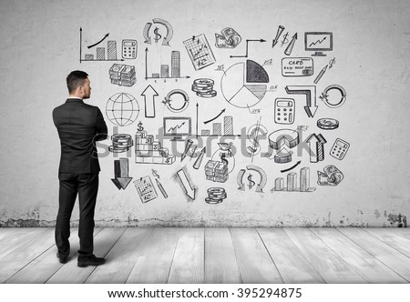 Back view man looking at white wall with hand-drawn sketches related to economics and statistics