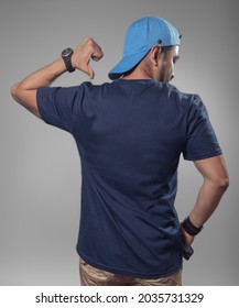 Back view of man. Mockup of male latin hispanic model wearing a navy blue t-shirt and blue cap pointing the back of his t-shirt on clear gray gradient background.