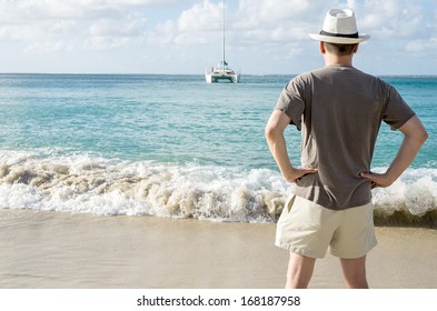 Back View Of A Man On A Beach Looking At A Catamaran