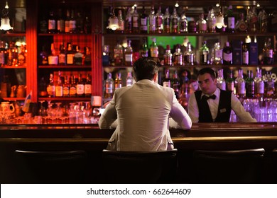 Back view of a man ordering drink to a bartender while sitting at the counter at the pub