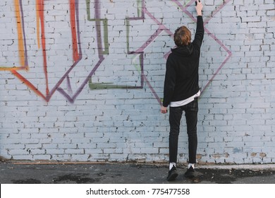 back view of man painting colorful graffiti on wall