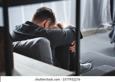 back view of man with panic attack crying and hugging legs in apartment 