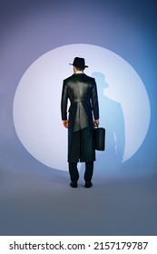 Back View Of Man Silhouette In Black Coat And Hat Holding Briefcase In The Spotlight On Studio Background. Noir Film Style. Private Detective, Spy, Investigation Concept