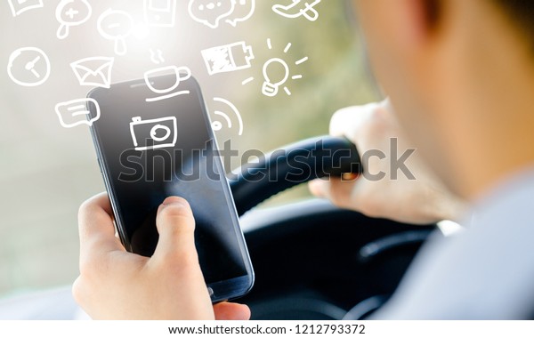 Back view of man sitting at car driver seat
and looking at dark screen of
smartphone