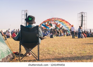 Back View Of Man Sitting Chair On The Grass, Enjoying An Outdoors Music, Culture, Community Event, Festival,Funny Group Of Young Girls And Boys At Music Festival, Happy Teen At Summer Festival.