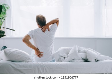 Back View Of Man Sitting On Bed And Suffering From Back Pain