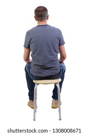 Back View Of A Man Sitting On A Chair. Rear View People Collection.  Backside View Of Person.  A Guy In A Gray Jacket Is Working Or Studying. The Guy In The Striped T-shirt Is Sitting On A Stool.