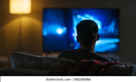 Back View of a Man Sitting on a Couch Watching Movie on His Big Flat Screen TV.