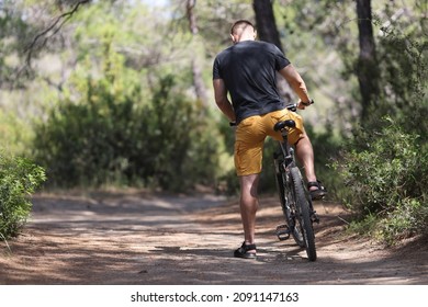 Back View Of Man Sitting On Bicycle On Forest Road