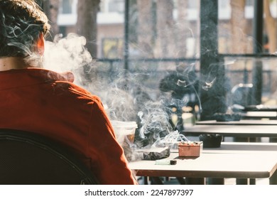Back view of man smoking tobacco cigarette in cafe. Unhealthy lifestyle. 