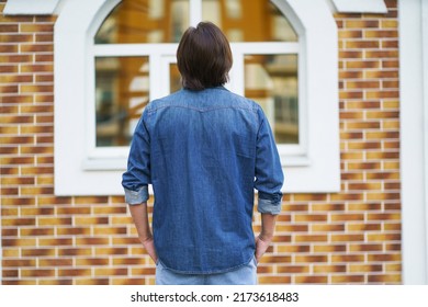 Back View Of A Man Standing Alone Looking At Old Town Building While Traveling In European Cities During Vacation Time Wearing Denim. Travel Concept. 