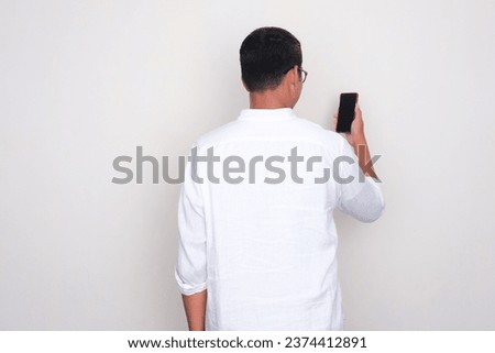 Back view of a man standing while looking to mobile phone screen that he hold