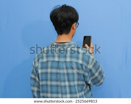 Back view of a man standing while looking to mobile phone screen that he hold