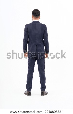 Back view of a man in a suit standing in front of a white background                         