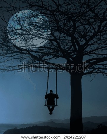 Back view of man swinging on the wooden swing on big leafless tree. Scenic landscape. view of unrecognisable man swinging on swing with rope under mountains. full moon behind branches. above mountains