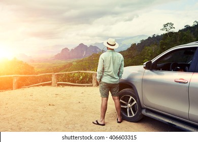 Back View Of A Man Is Thinking About This Amazing World, While Is Standing On A Mountain Against Jungle View. Young Male Traveler Is Enjoying Beautiful Landscape During Road Trip On Suv In Thailand