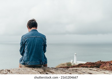 Back View Of Man Traveller, Who Is Standing On Edge Of The Cliff On Irish Sea And Is Doing Photos On Smartphone. Amazing View During Staycation And Travelling In UK, Anglesey, South Stack Lighthouse