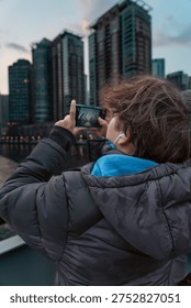 Back view of a man using a smartphone to photograph the illuminated downtown skyline of Chicago at night. Bright city lights and modern skyscrapers glowing in the evening vertical view