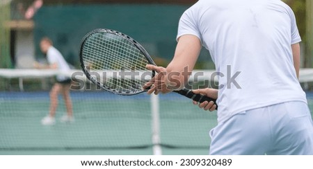 Back view of man waiting to receive the ball, tennis players playing a match on the court in sunny day.