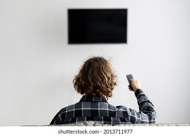 Back View Of Man Watching Television Pointing TV Remote Control On Flatscreen Plasma Set With Empty Screen, Sitting On Sofa At Home. Unrecognizable Guy Watching Movie On Weekend. Selective Focus