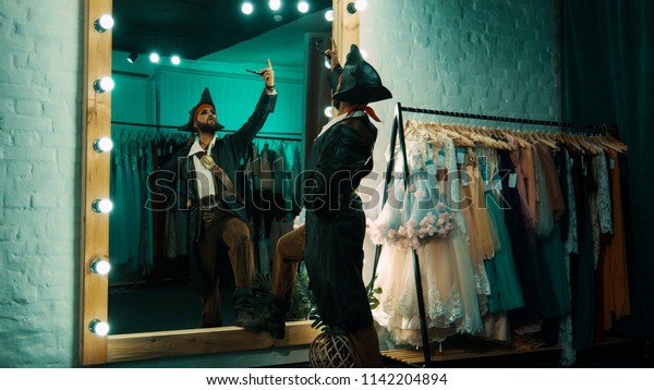 Back view of man wearing costume of pirate\
and standing in front of mirror in dressing room practicing scene\
from performance