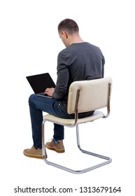 Back View Of A Man Who Sits On A Chair With A Laptop.  Rear View People Collection.  Backside View Of Person.  Isolated Over Whit. A Man In A Gray Jacket Sits On A White Chair And Typing On A Laptop.