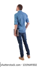 Back View Of A Man Who Is Standing With A Laptop. Rear View People Collection.  Backside View Of Person.  Isolated Over White Background. Young Engineer With A Closed Laptop In Hand.