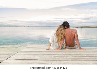 Back view of a man and woman couple sitting on a Jetty under a blue cloudy sky