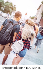 Back view of man and woman holding hands and walking on street with backpacks 