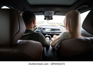 Back view of man and woman traveling in car. Beautiful young couple sitting on front passenger seats, handsome man driving comfortable automobile. Woman pointing on the way. - Powered by Shutterstock