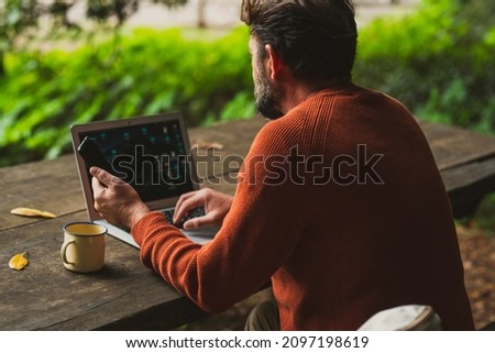 Back view of a man working with mobile phone and laptop computer in outdoors. Wireless and roaming internet wifi connection and people using technology for online job and smart working